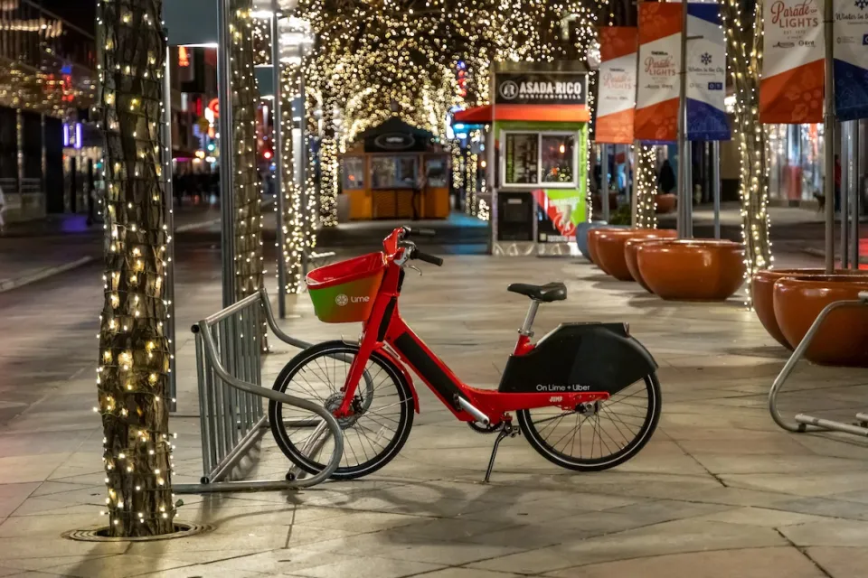 Lime rental bike on sidewalk in Denver, Colorado with Christmas lights in background.